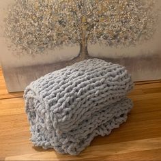 a blue knitted blanket sitting on top of a wooden floor next to a painting