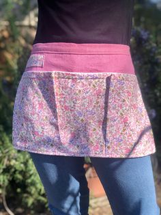 the back of a woman's pink apron with floral print on it and blue jeans