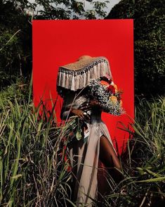 a woman standing in tall grass next to a red box with flowers on it's head