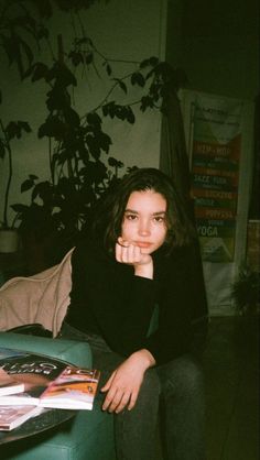 a woman sitting on top of a green couch next to a potted plant in a living room