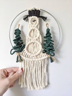 someone is holding up a macrame wall hanging with pine trees on the hoop