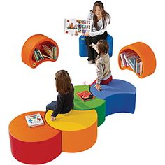 three children sitting on different colored tables and chairs with bookshelves in the background