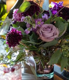 a glass vase filled with purple flowers on top of a wooden table next to two glasses