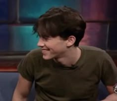 a young man sitting on top of a blue couch next to a tv screen and smiling