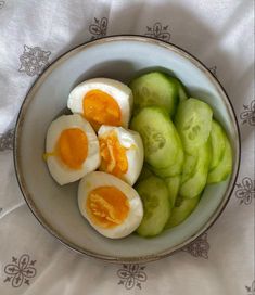 a bowl filled with hard boiled eggs and cucumbers on top of a white table cloth