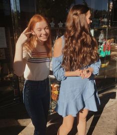 two young women walking down the street talking to each other and one has her hand on her head