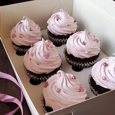 six cupcakes in a box with pink frosting on them and a ribbon