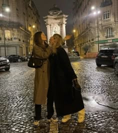 two women standing in the middle of a cobblestone street with a clock tower in the background