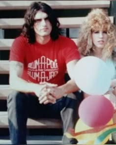 a man and woman sitting on a bench next to each other with balloons in front of them