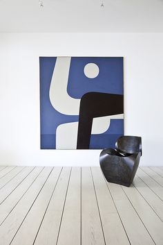 an abstract painting hangs on the wall next to a black chair in a white room