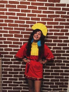 a woman in a red and yellow costume standing next to a brick wall with her hands on her hips