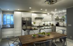 a modern kitchen with stainless steel appliances and wooden dining table surrounded by white chairs, an island that has fruit on it