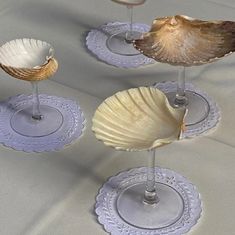 three seashells sitting on top of wine glasses and saucers, one is empty