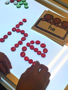 a child is playing with buttons on a white table and the letters h are spelled out