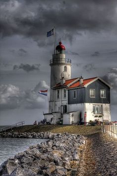 a lighthouse on the edge of a body of water with clouds in the sky above it