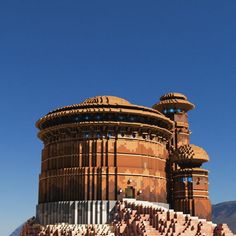 a large building made out of bricks on the side of a hill with mountains in the background