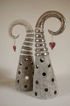 two vases with hearts hanging from them on a white tablecloth covered surface, one is made out of cement and the other has a metal spiral design