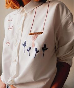 a woman wearing a white shirt with embroidered flowers on the front and side, holding her hands in her pockets