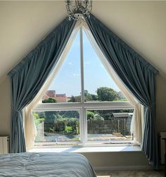 a bed sitting under a large window next to a chandelier in a bedroom