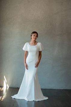 a woman in a white dress standing on a wooden floor with her hands on her hips