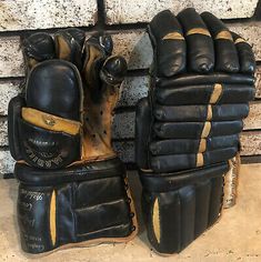 two black and gold gloves sitting next to each other on a brick wall in front of a