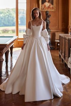 a woman in a white wedding dress standing on a wooden floor with an ornate chandelier