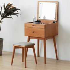 a wooden dressing table with mirror and stool next to potted plant on the floor