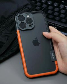 an orange iphone case is held up by someone's hand near a computer keyboard