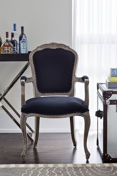 a chair sitting in front of a table with bottles on it and a bookcase