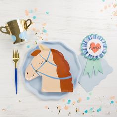 a paper plate with a horse on it next to a gold cup and award ribbon