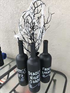 three black vases sitting on top of a table with dead branches in them and writing on the bottles