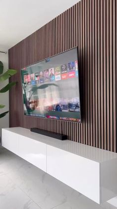 a flat screen tv sitting on top of a white shelf in front of a plant