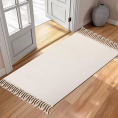 a white rug with fringes on the floor next to an open door and vase