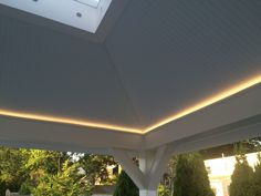 the inside of a covered patio area with lights on and trees in the back ground