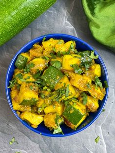 a blue bowl filled with food next to a zucchini and cucumber