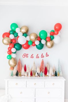 a white dresser topped with lots of balloons and christmas tree decorations on top of it