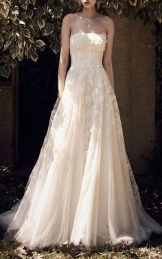 a woman standing in front of a tree wearing a wedding dress with flowers on it