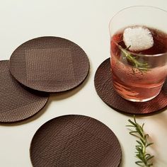 four brown coasters on a white table with a drink and rosemary sprig