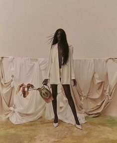 a woman with long hair standing in front of white drapes and holding a vase