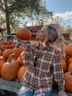 a woman sitting on a wooden bench surrounded by pumpkins