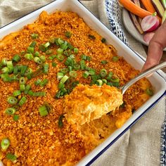 a casserole dish with green onions and cheese being spooned into the casserole