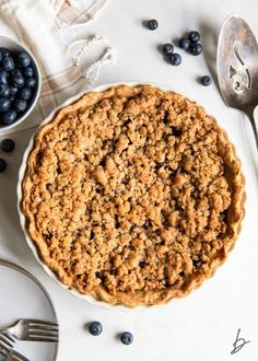 an oatmeal pie with blueberries on the side next to a fork and spoon