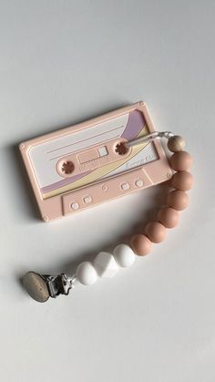 an old fashioned tape recorder and beaded bracelet on a white surface with a pink background