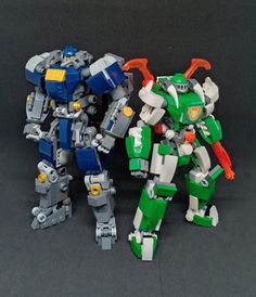 two toy robots standing next to each other on a black surface with one robot facing the camera