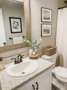 a white toilet sitting next to a sink in a bathroom under a mirror and framed pictures on the wall