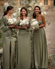 three bridesmaids standing in front of an arch with flowers and greenery on it