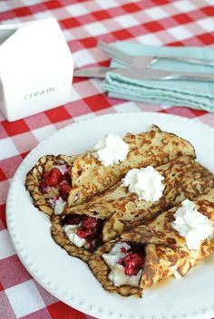 a white plate topped with pancakes covered in whipped cream and strawberries on top of a checkered table cloth