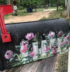 a mailbox with flowers painted on it sitting on a wooden table in front of a fence