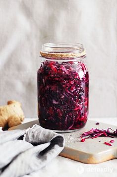 a jar filled with red cabbage sitting on top of a table next to a cutting board