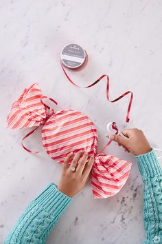 someone is sewing something on the table with some scissors and tape around it that has been wrapped in red and white stripes